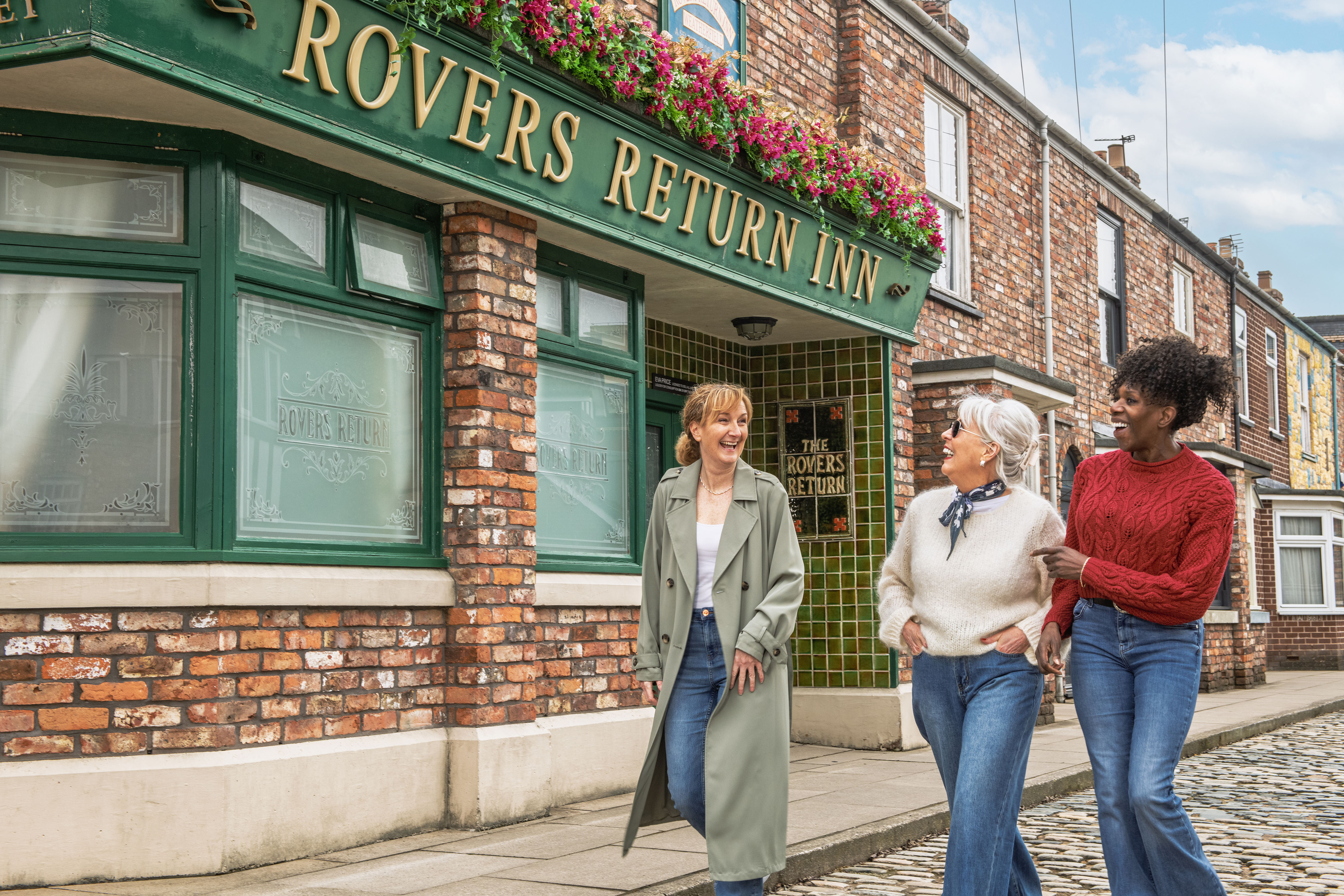 Three friends walking past the Rovers Return pub on the cobbles at the Coronation Street Experience