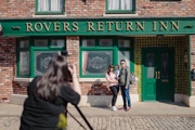 A couple with their toddler posing for a photo in front of the Rovers Return Inn at the Coronation Street Experience in Manchester