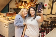 Two guests taking a selfie inside the Roy’s Rolls interior set at the Coronation Street Experience in Manchester