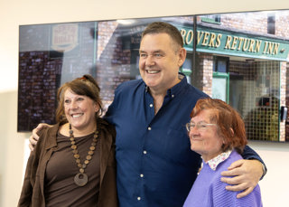 Tony Maudsley poses with happy fans on either side during a Star Tour at the Coronation Street Experience 