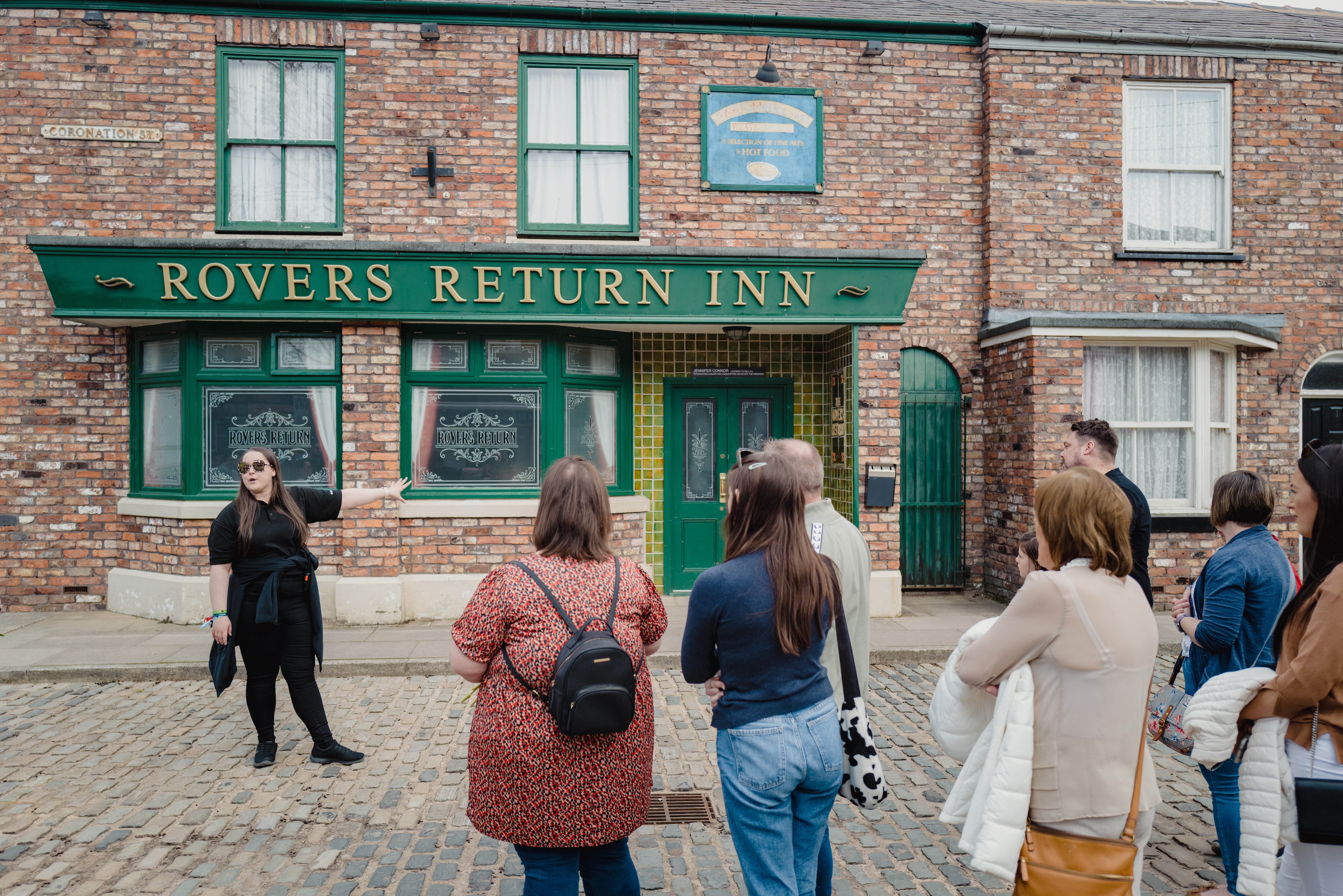 A tour guide speaking to visitors in front of the Rovers Return Inn at the Coronation Street Experience in Manchester