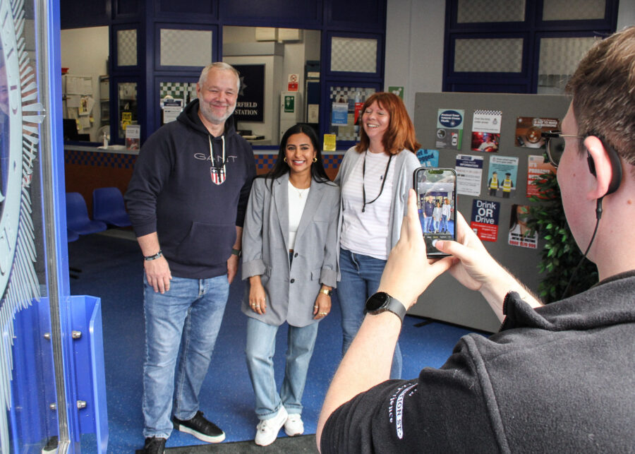 A tour guide of the Coronation Street Experience taking a phone picture of Sair Khan and a couple of guests.