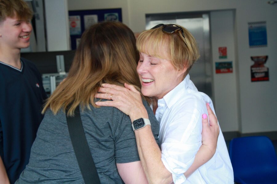 Sally Dynevor warmly hugging an elated guest, with the guest's son smiling in the backdrop, all set within the Weatherfield Police Station.